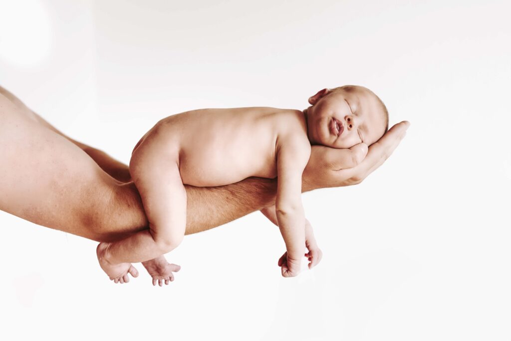 Nacktes baby liegt auf Papas Hand und schläft.