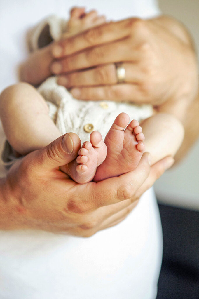 Hände in denen nachte Babyfüße sind.