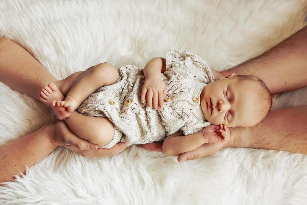 Eltern halten ein Baby in den Händen. Der Junge schläft und wird von oben fotografiert.