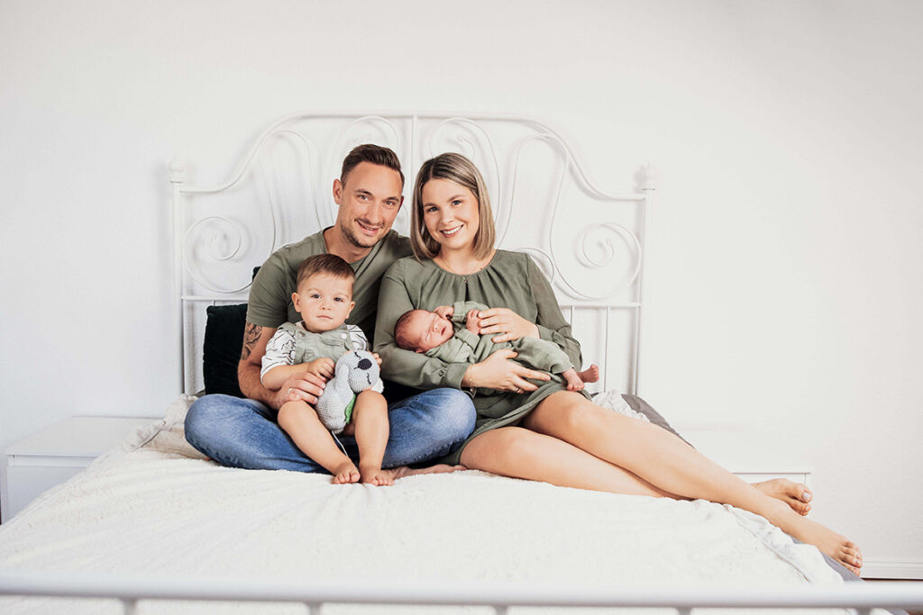 Familie sitz im Bett und hält das Baby im Arm.
