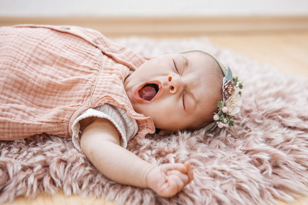 Baby Mädchen liegt auf dem Rücken mit Haarband und Gähnt.