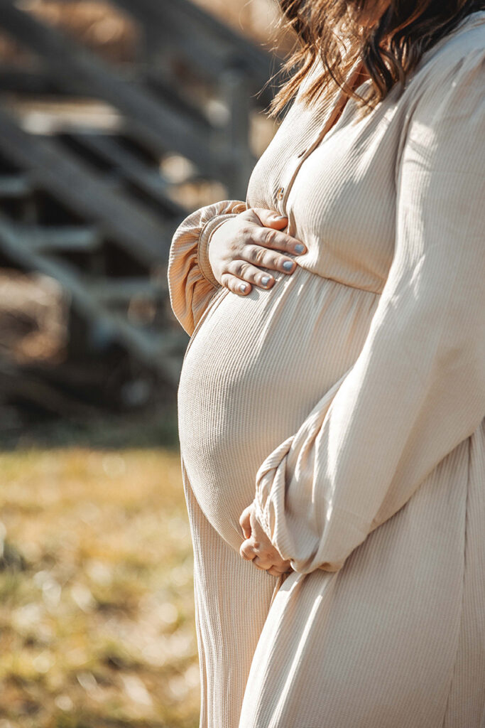 Babybauch als Nahaufnahme vor einer Holzbrücke.