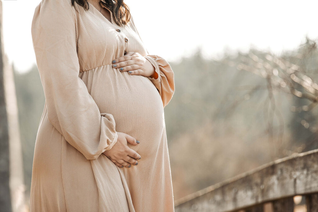 Zeigt  ein Babybauch als Nahaufnahme auf einer Brücke.