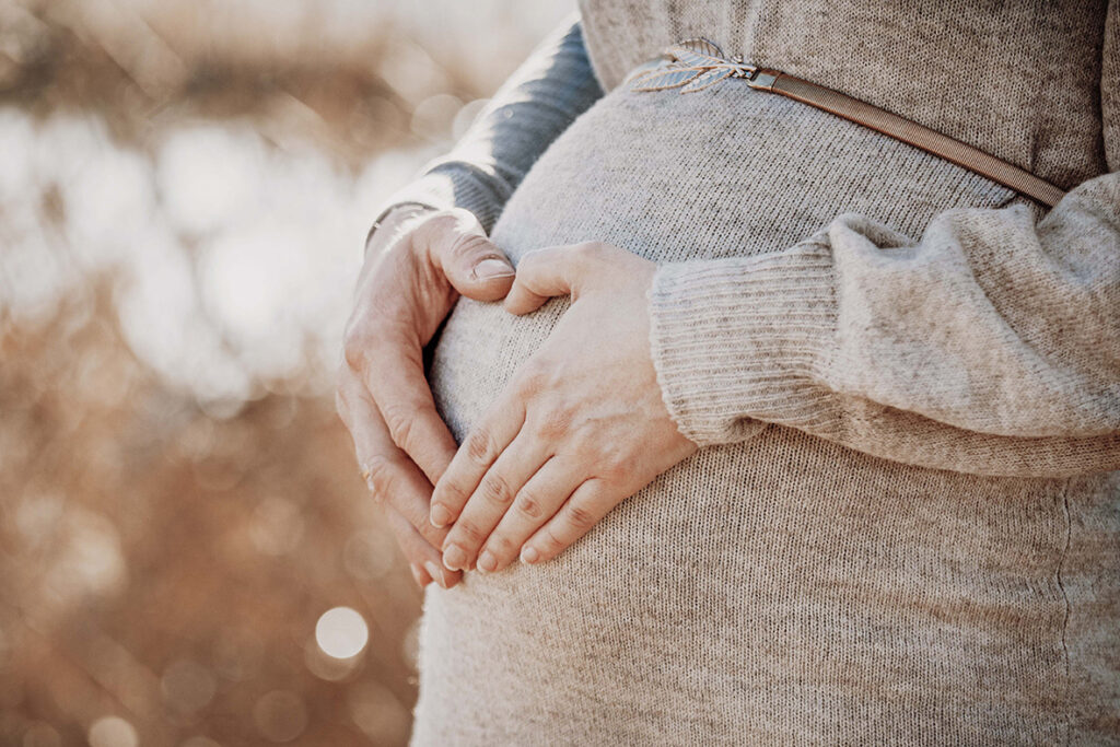 Babybauch mit Mama und Papa Hand die ein Herz formen.