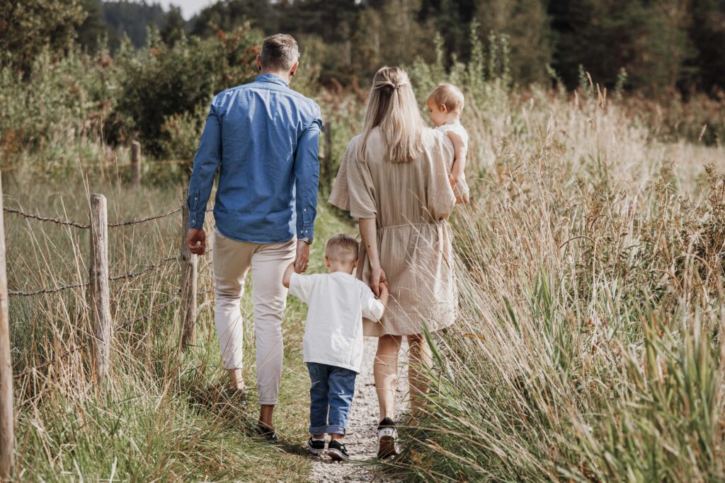Vier Köpfige Familie geht Hand hin Hand einen kleinen weg entlang. Das Bild zeigt sie von Hinten.