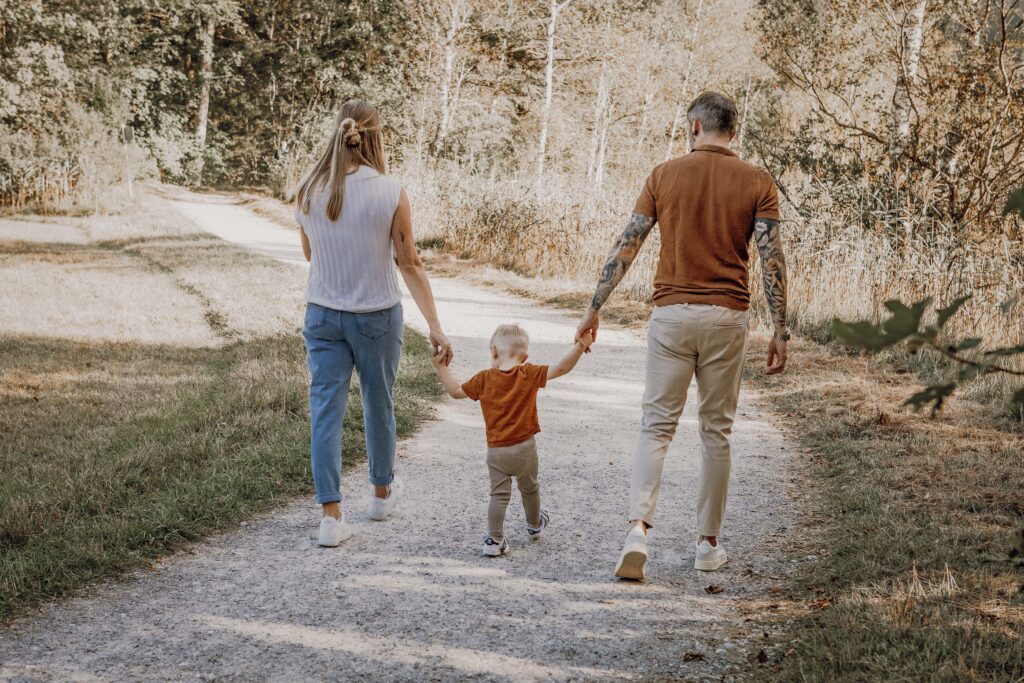 Familie geht Hand in Hand einen Weg am Waldrand entlang in Füssen.