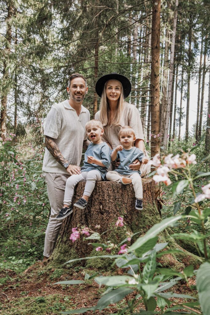 Familie farblich abgestimmt steht im Wald. die Kinder sitzen auf einem Baumstamm.