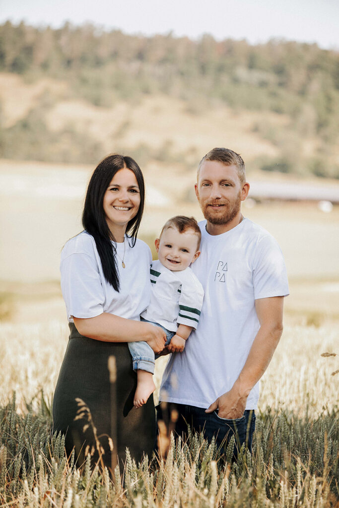 Familie Steht im hohen Feld mit klein Kind auf dem arm. alle Tragen weiße T-Shirt und lachen.
