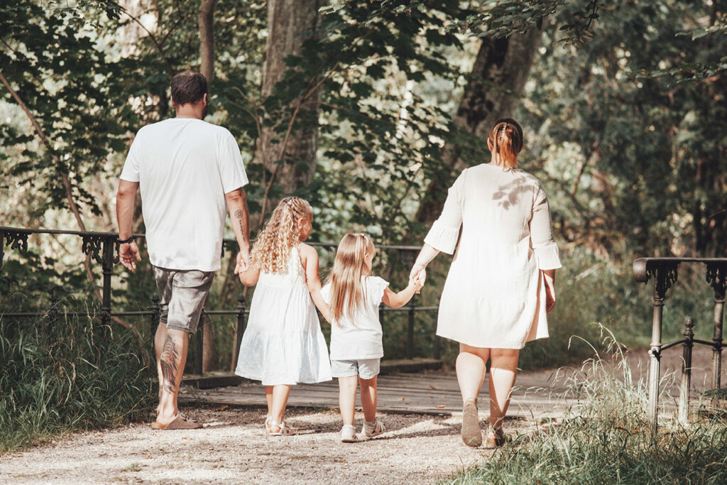 Eine vierköpfige Familie geht Hand in Hand im wand einen weg entlang im Sommer.
