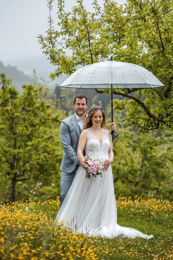 Brautpaar steht hintereinander unter dem Regenschirm.Klosterkirchberg.