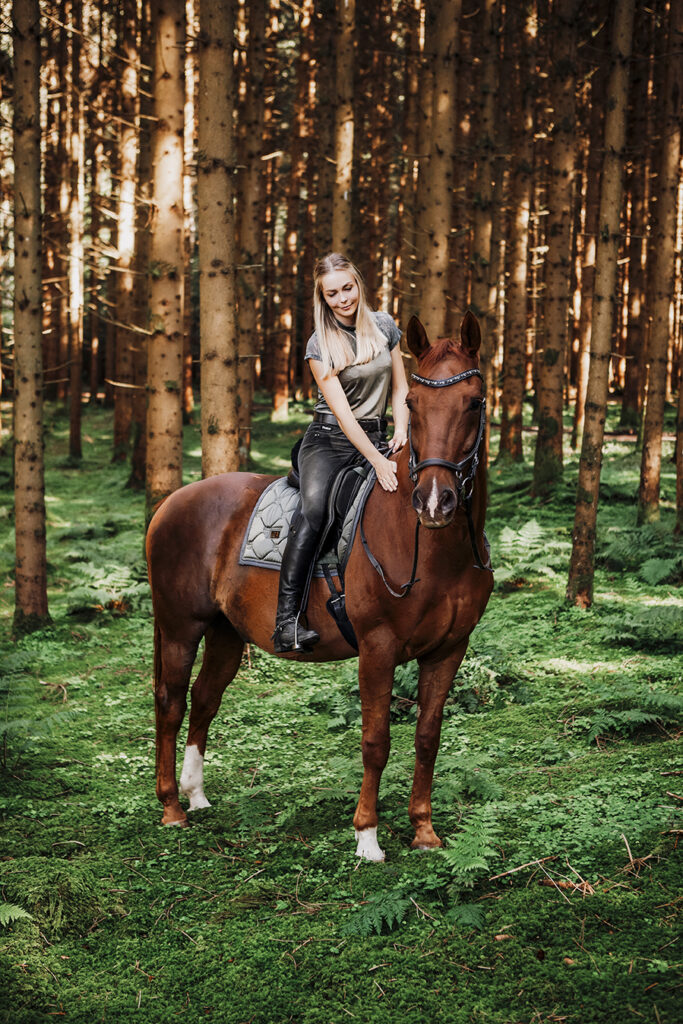 Blonde Frau sitzt auf einem Braunes Pferd im Wald . Allgäu Füssen.