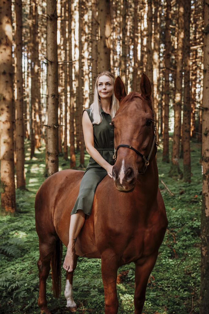 Blonde Frau sitzt in Grünen Kleid auf einem Braunes Pferd im Wald . Allgäu Füssen.