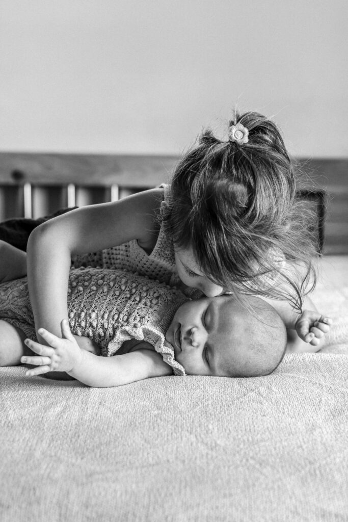 Große Schwester liegt mit dem Baby auf dem Bett und Küsst es, Bild ist Schwarzweiß. Sigmaringen.