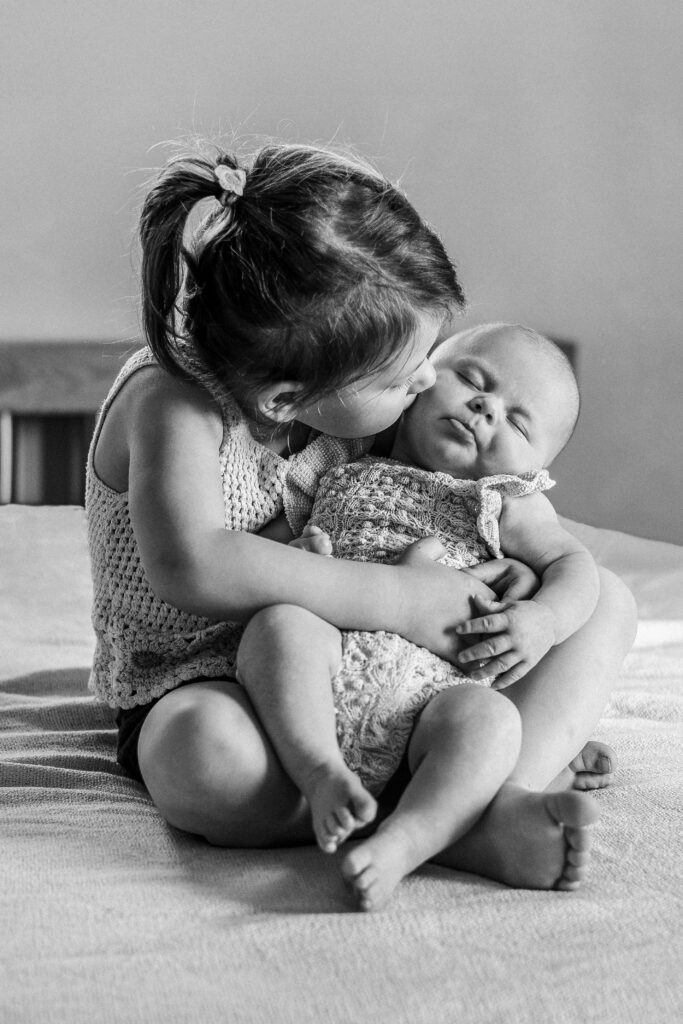 Große Schwester hat das Baby im Schoß und schaut es an. Sigmaringen.