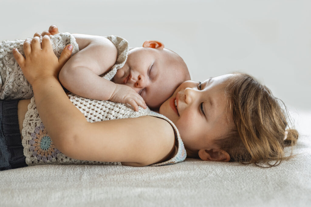 Große Schwester hat das Baby auf dem Bauch liegen und Küsst es auf den Kopf. Empfingen.