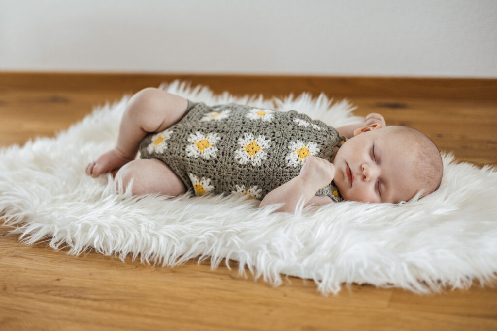 Baby liegt auf dem Fell und hat einen Grünen Strampler an. Sigmaringen.